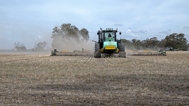 A tractor plowing an agricultural field in Devenish, VIC, Australia under a cloudy sky.