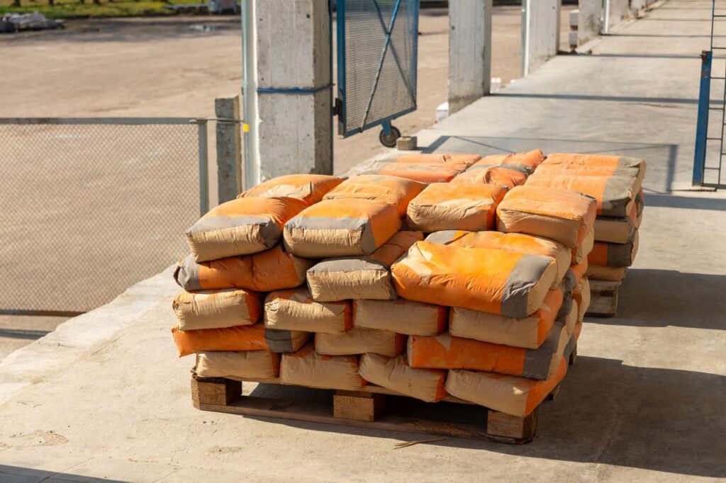 pexels-photo-29817952-29817952 Pile of orange cement bags on a wooden pallet in an industrial setting.