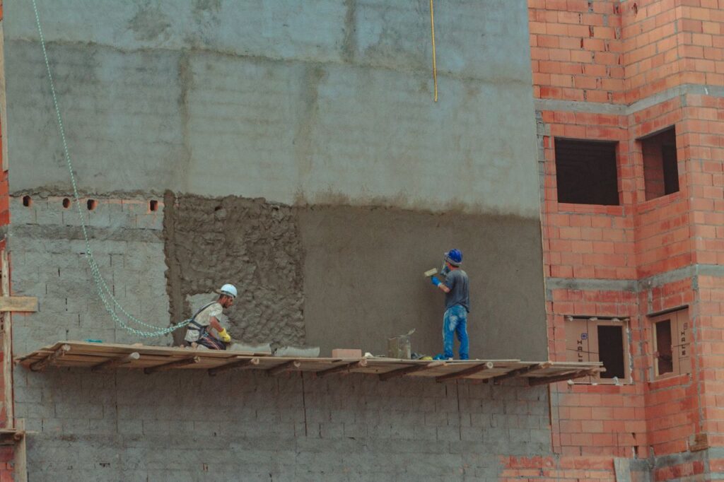 pexels-photo-5242049-5242049 Exterior of industrial construction with wooden site on brick wall and builders in protective hard hats